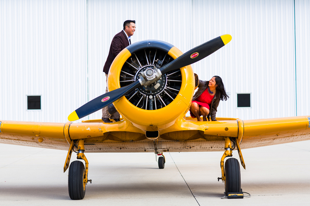 Couple stands on a yellow WWII plane during an airport engagement session