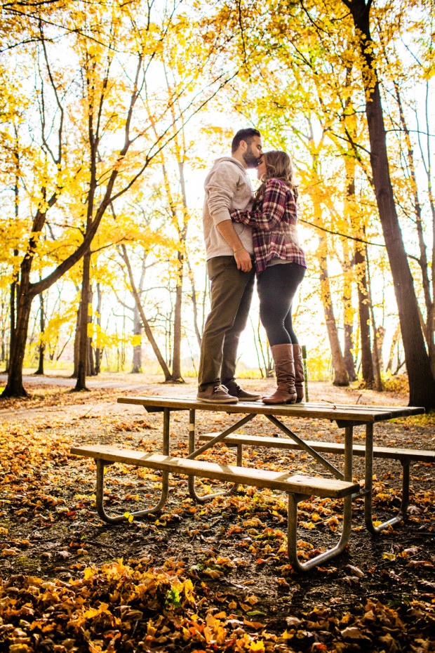 A couple stands on a picnic table during a campground during their fall engagement session 
