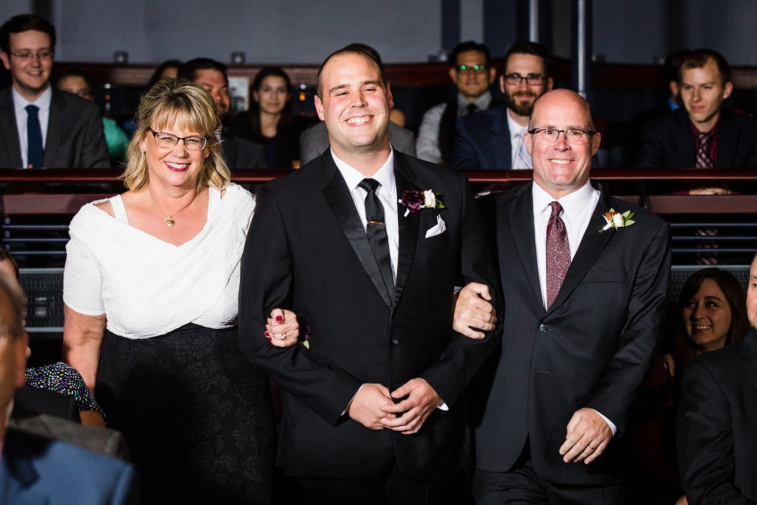 A groom walks down the aisle with his parents at a Mayne Stage wedding in Chicago. 