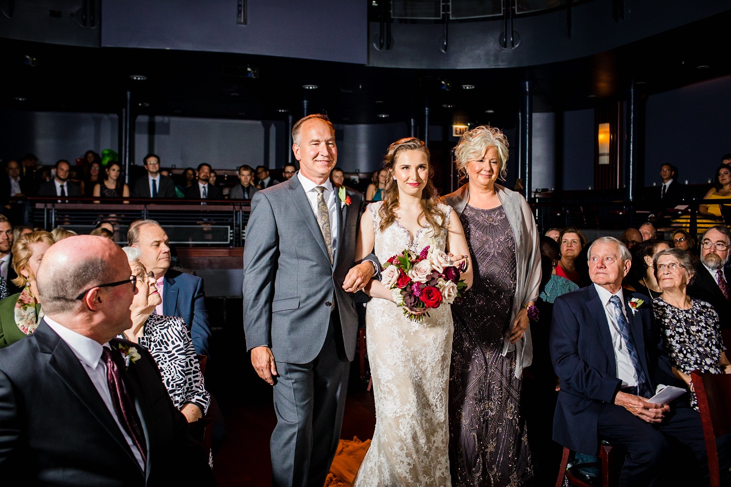 A bride walks down the aisle with her parents at a Mayne Stage wedding in Chicago. 