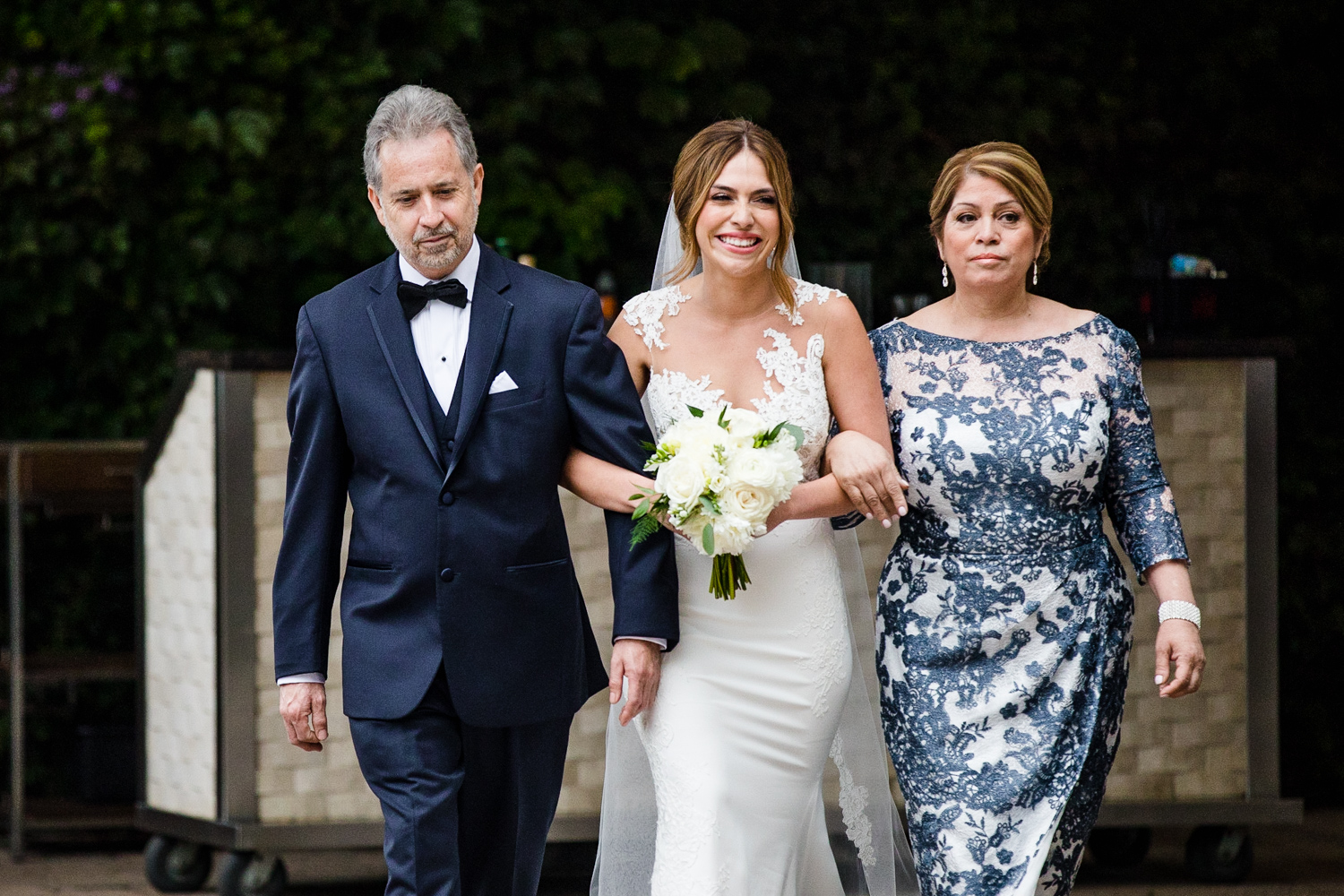 A bride walks down the aisle with her parents during a Gallery Marchetti wedding.