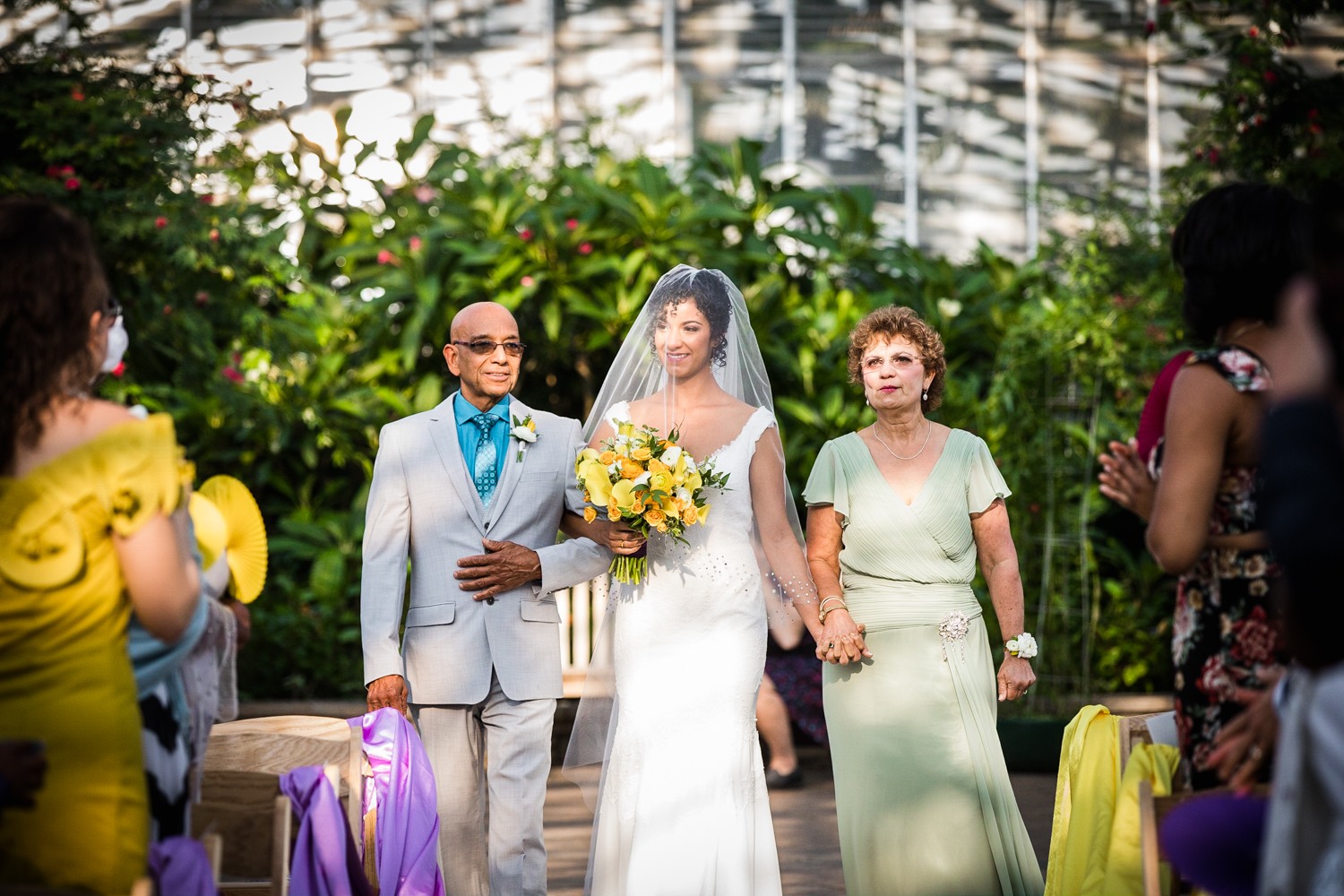 A bride walks down the aisle with her parents at a Garfield Park Conservatory wedding.