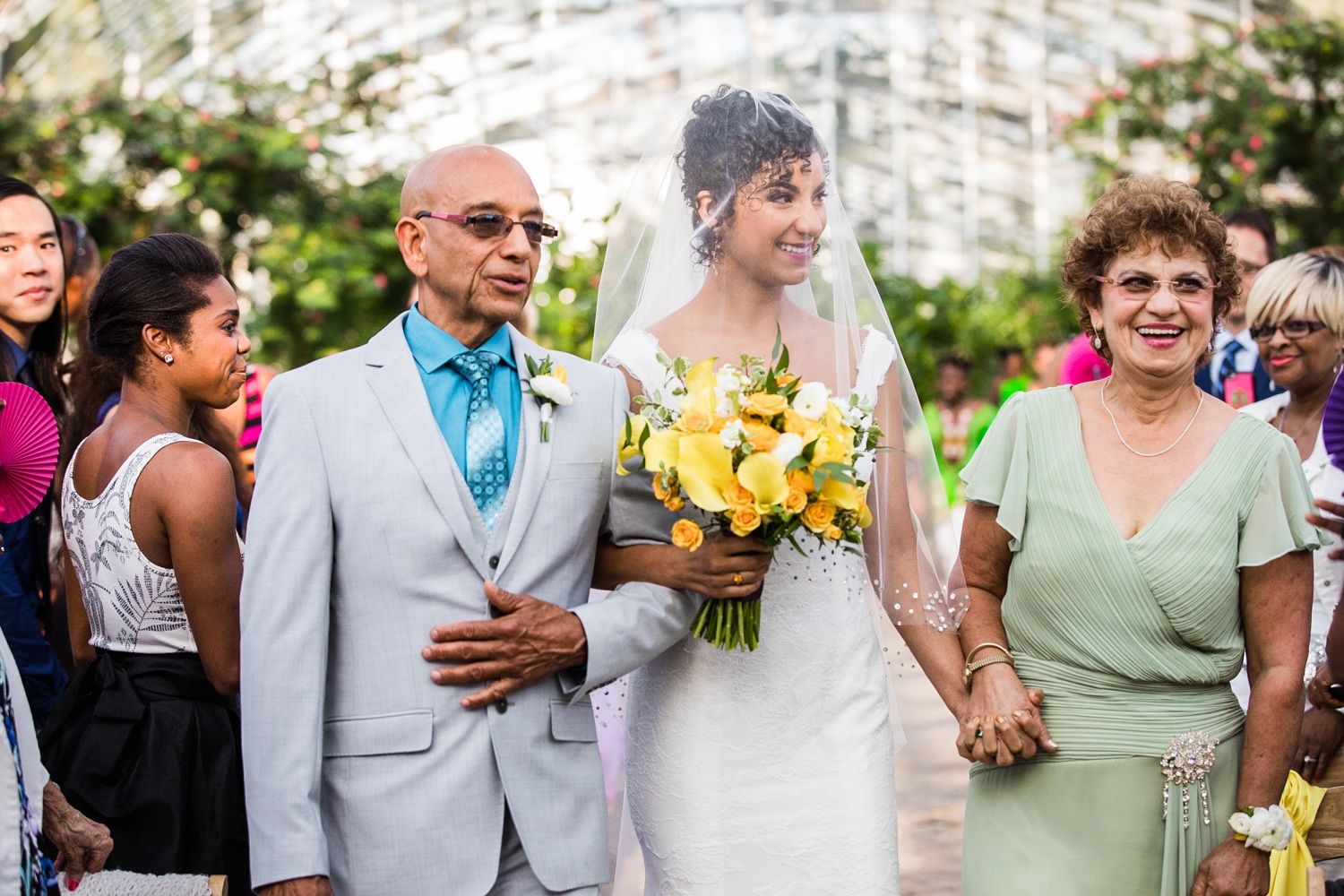 A bride walks down the aisle with her parents during her Garfield Park Conservatory wedding.