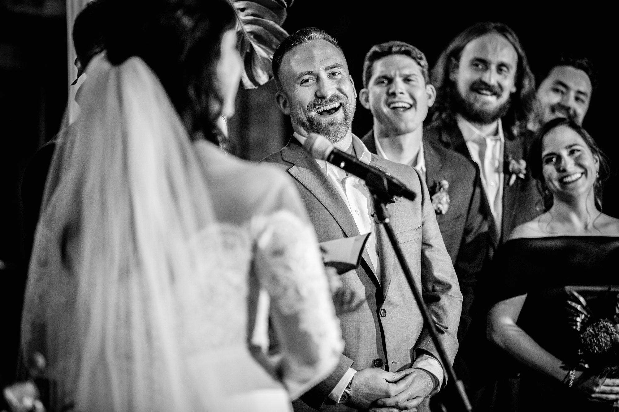 The groom and wedding party laugh while listening to the bride's vows at a Salvage One wedding. 