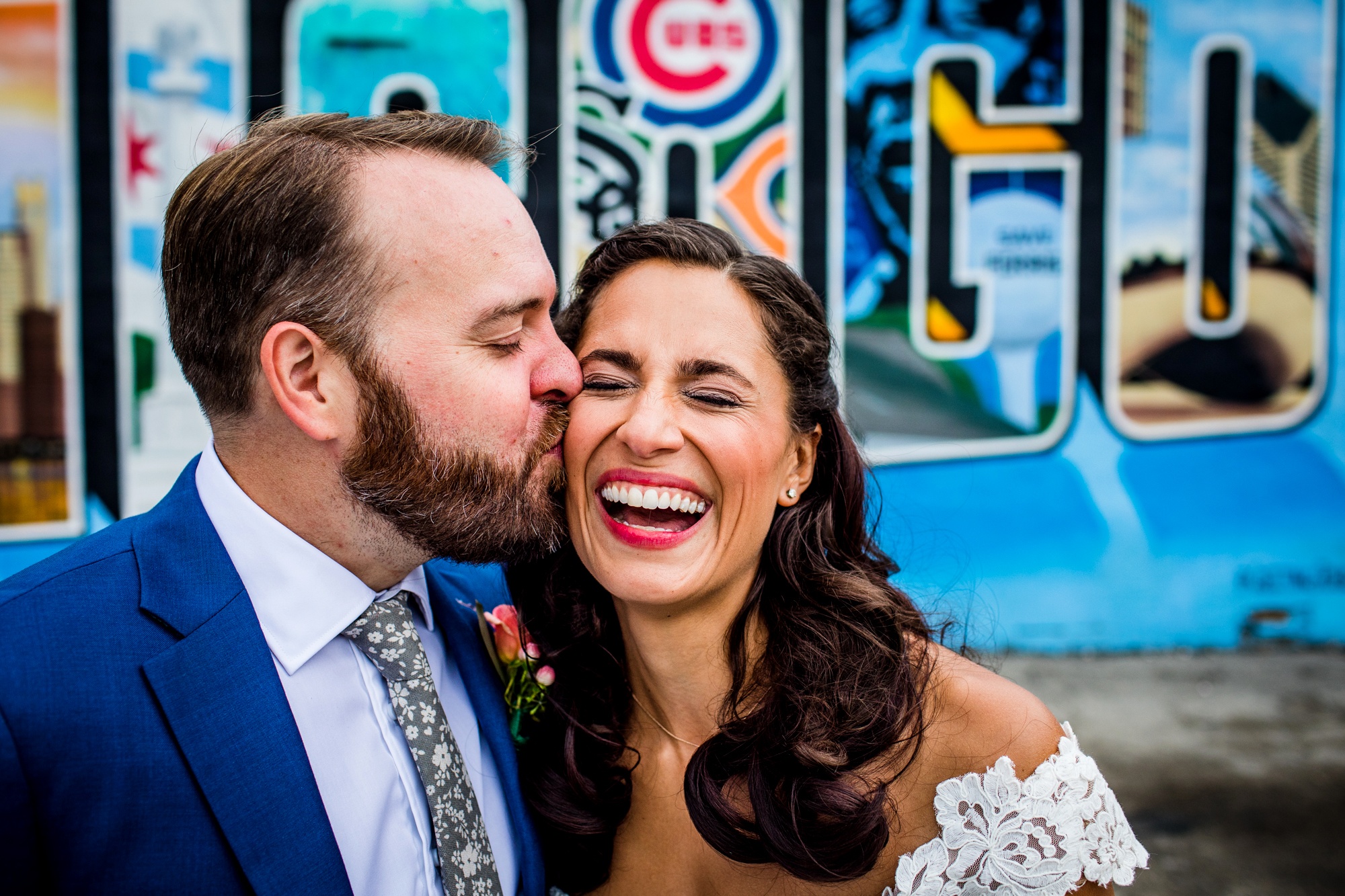 A groom kisses his bride on the cheek in front of the Chicago mural in Logan Square.