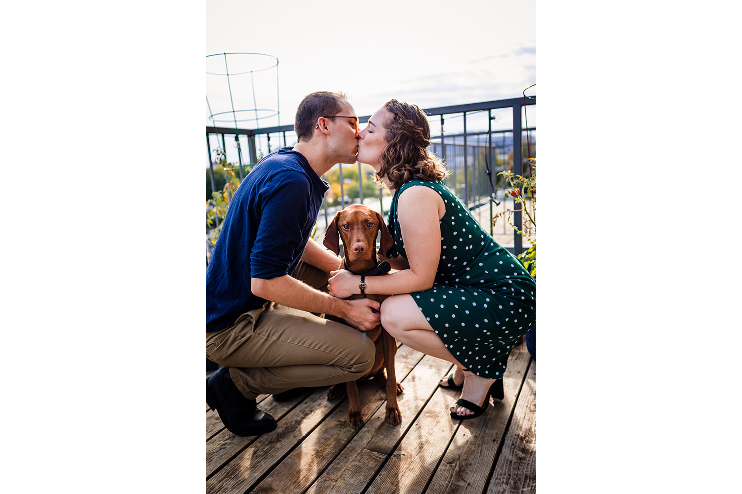 A couple kisses each other with their dog during a rooftop engagement session in the West Loop.