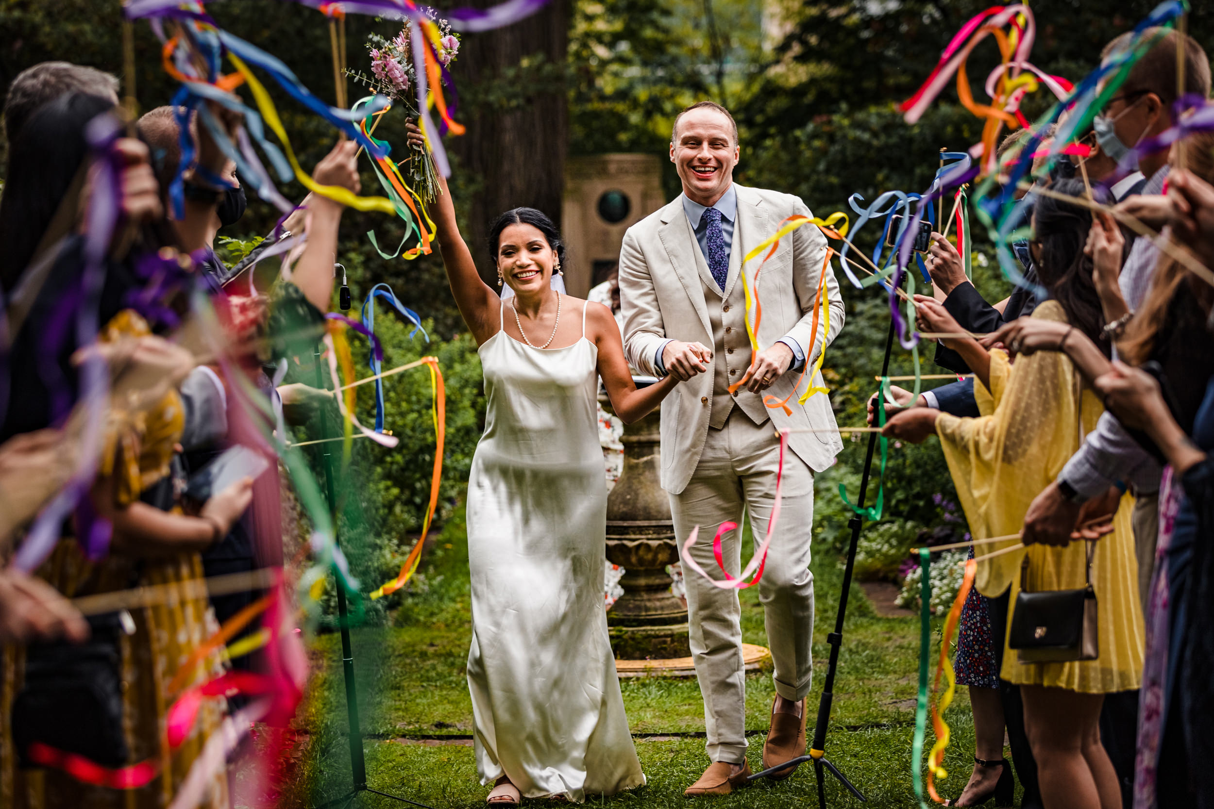 A couple walks down the aisle as guests wave streamers during a Shakespeare Garden micro wedding in Evanston.