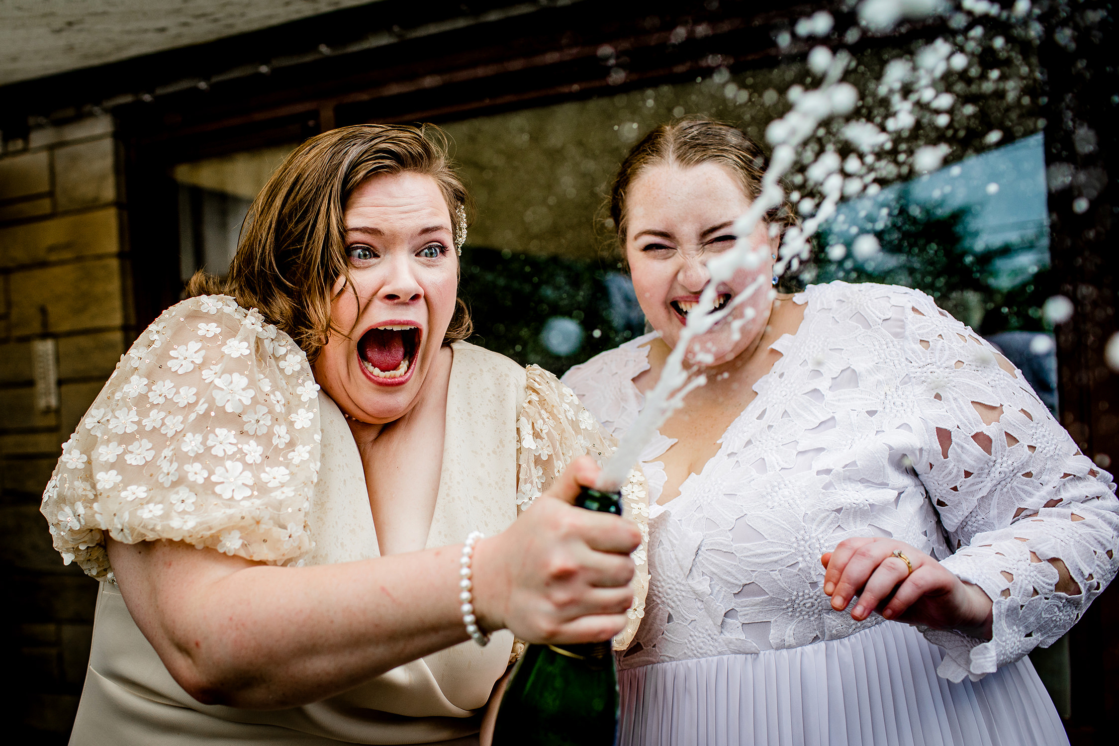 Brides laugh as they pop a bottle of champagne after their New Lenox backyard wedding. 
