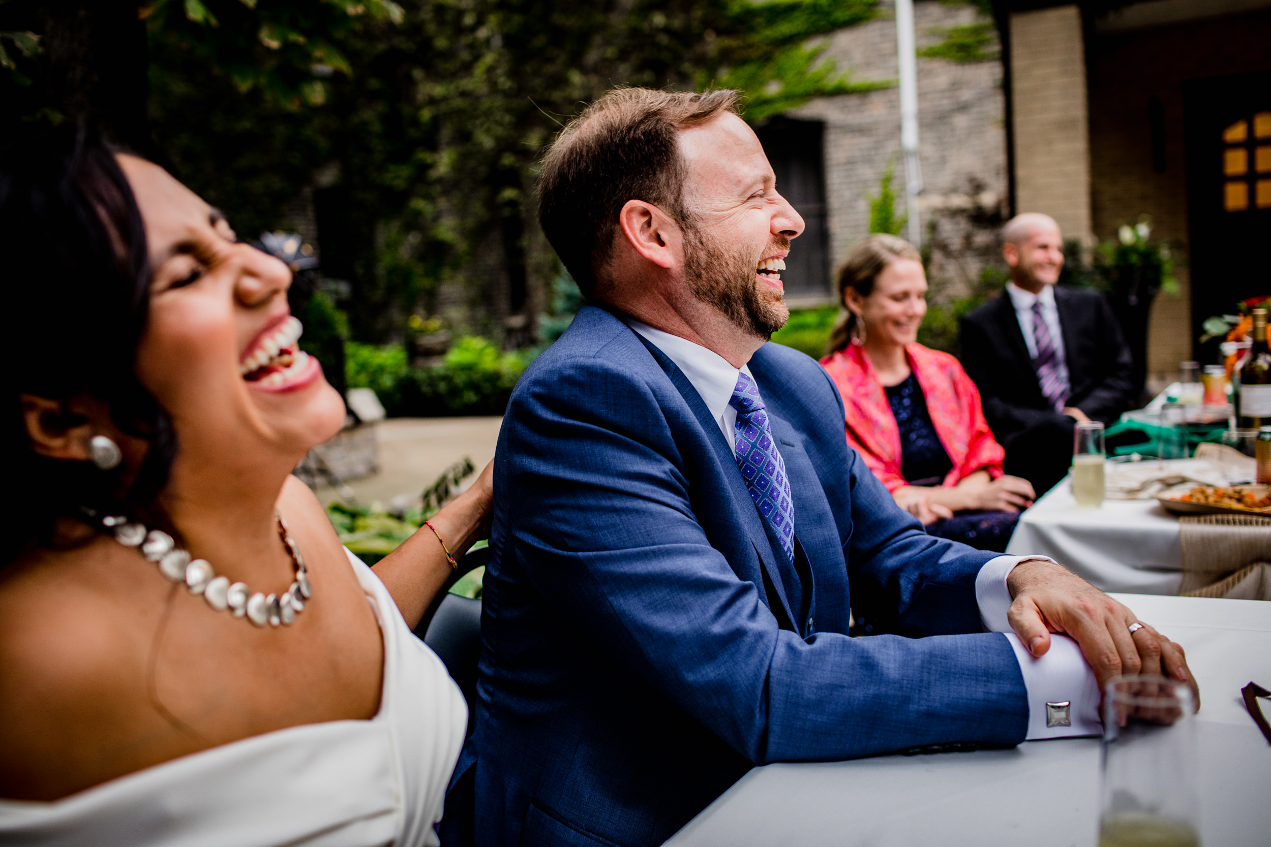A couple laughs at a wedding toast during their Church of the Ascension garden wedding reception. 