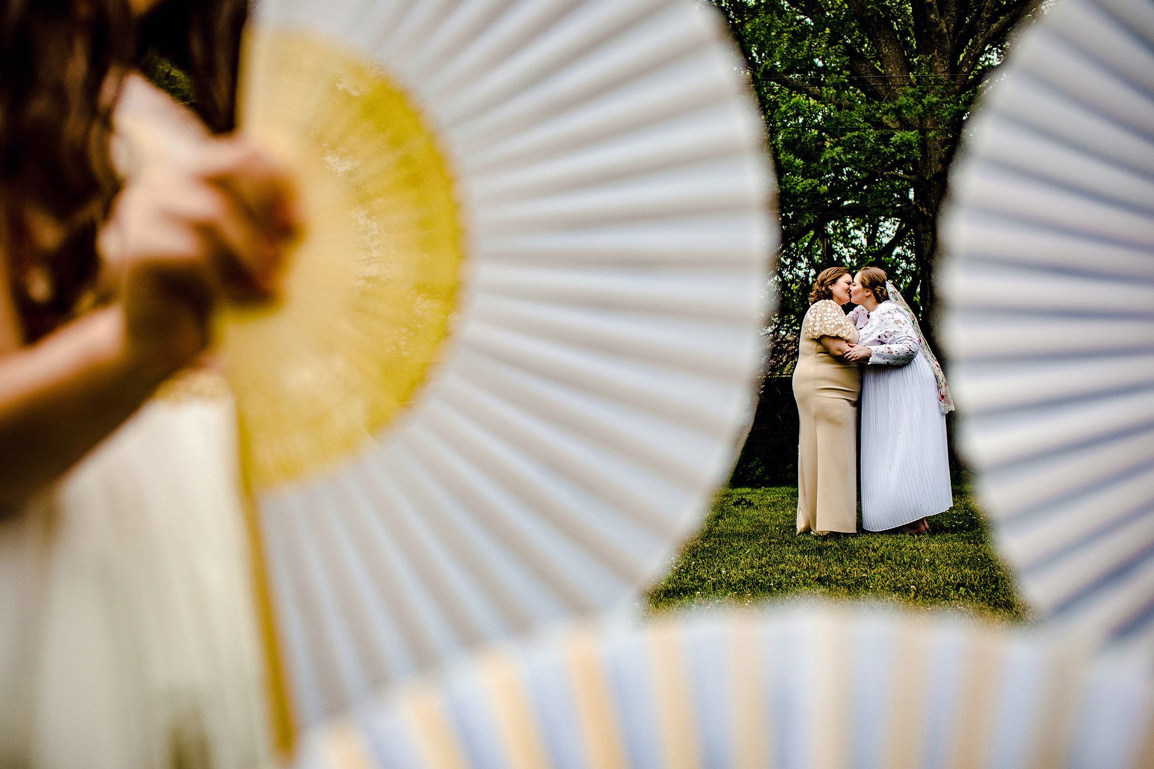 Brides kiss while a flower girls waves a fan at a backyard wedding in New Lenox, Illinois.